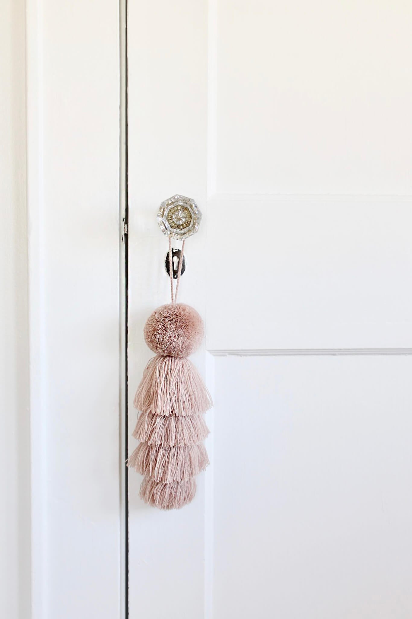 Blush pink tassel on glass door knob in white baby girl nursery interior