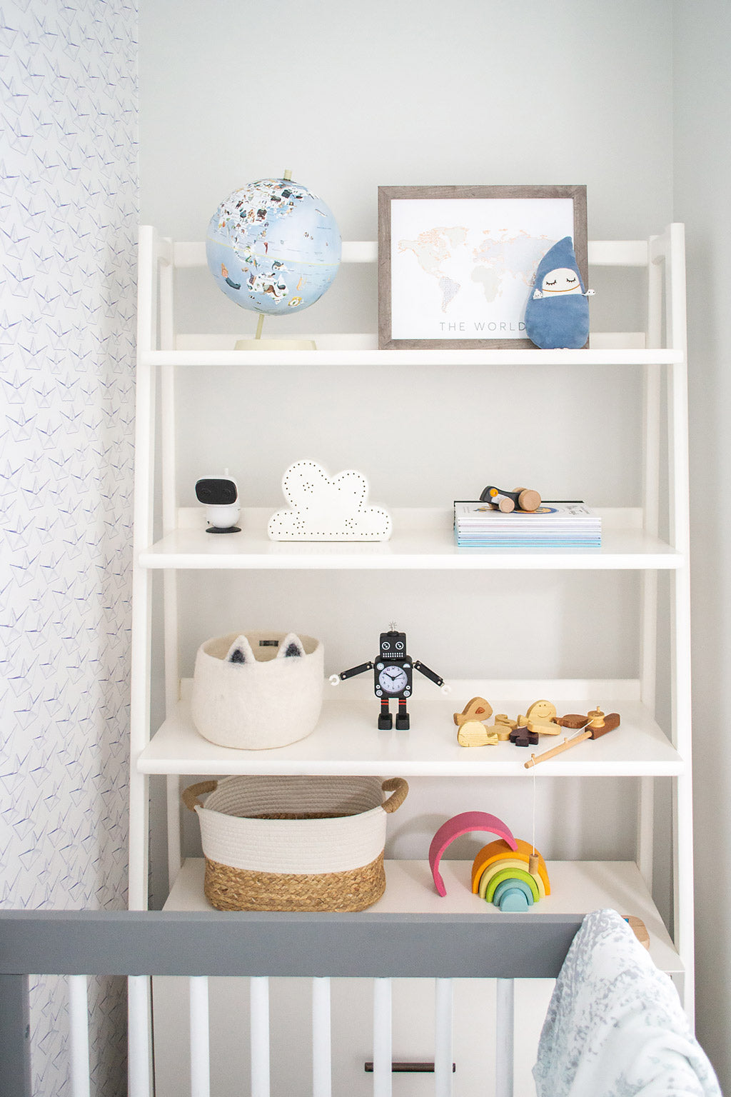 White ledge shelf with colorful nursery decor and books in white coastal baby boy nursery with paper boats removable wallpaper by Livettes