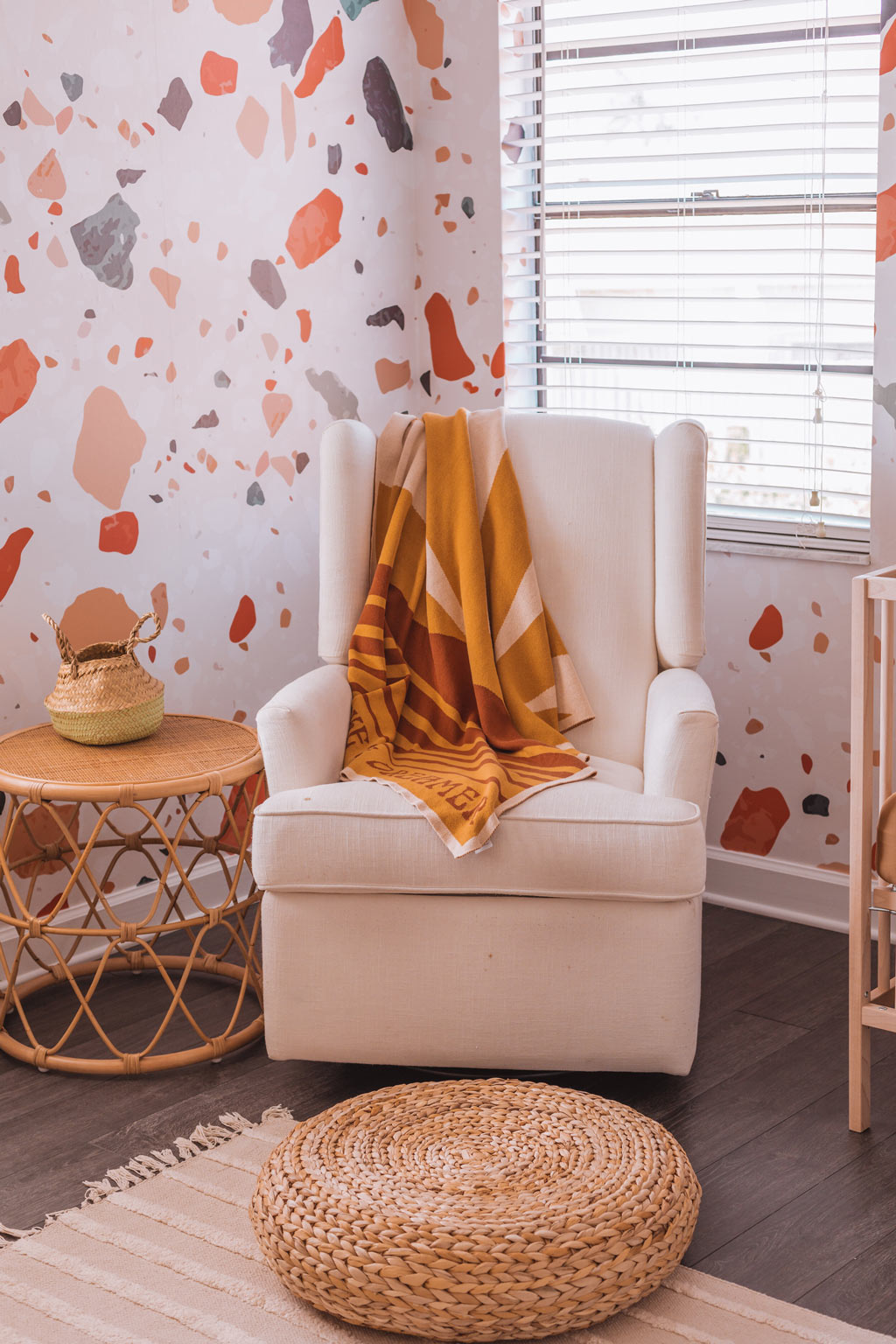 Gender neutral nursery rocking chair corner with terrazzo wallpaper feature wall, warm tone interior decor and woven basket organisation