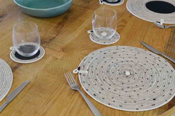 Mia Melange placemats in black and white, styled on a dining table. Mia Melange products available at Sarza home goods and furniture store in Rye New York.