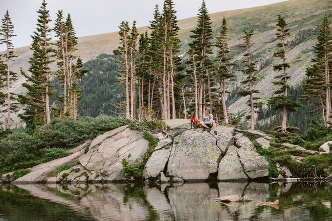 Nathan and Turkey sit on a rock next to an alpine lake.