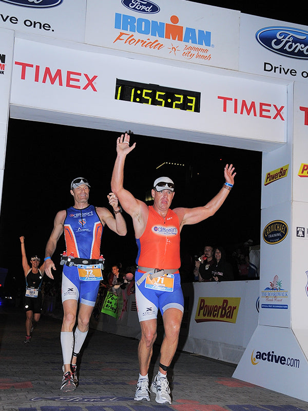 Richard running across the finish line of an iron man with his human guide.