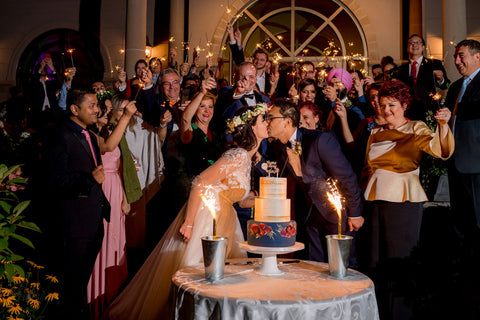 Henkaa A Bride's Story: Diana & Jas. Bride and groom kiss over wedding cake. Guests with sparklers.