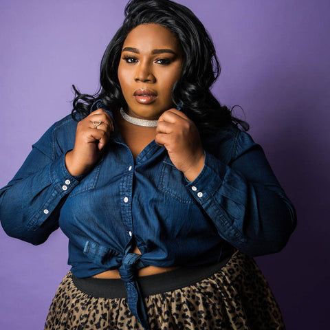 Woman modelling jean shirt and leopard print skirt against purple backdrop.