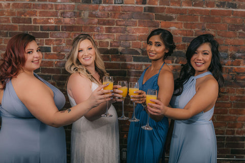 Bridesmaids and bride cheers with mimosas. Bridesmaids are wearing Henkaa Dusty Blue and Light Sky Blue Sakura Maxi infinity dresses and Slate Blue Ivy Maxi convertible dresses. Bride is wearing the Sakura Lace convertible wedding dress. 