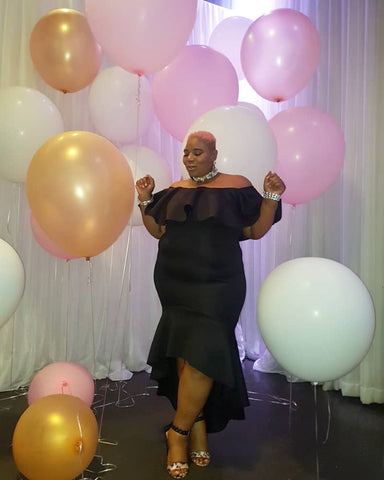 Women in black off-the-shoulder dress with pink, white and gold balloons.