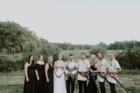Alex and Lauren Melnik stand with the bridal party and groomsmen. Bridesmaids in Henkaa Night Black Sakura Maxi infinity dresses and groomsmen in traditional medieval clothing with swords.