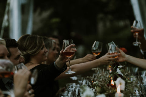 Attendees at a medieval themed wedding cheers with their glasses over harvest table.
