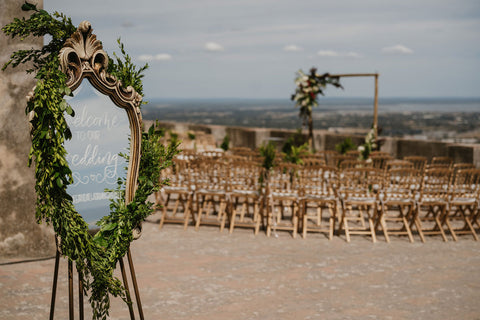 Ceremony setup featuring a mirror welcomine sign, semi-circle seating and a floral arch all atop the Pousada Castelo Palmela in Palmela, Portugal.