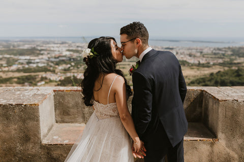 Bride and groom hold hands and kiss with the Palmela Portugal landscape in front of them.