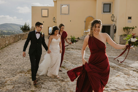 Bride and groom hold hands walking, bridesmaids are wearing Henkaa handmade in Canada Convertible Dresses in Burgundy Wine.