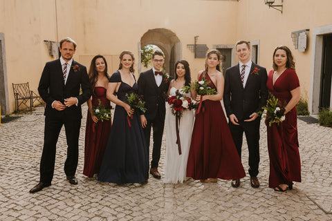 Bride and groom pose for a photo with their wedding party at the Pousada de Palmela in Portugal. Bridesmaids are wearing Henkaa Sakura Maxi Convertible Dresses in Burgundy Wine and Navy Blue.