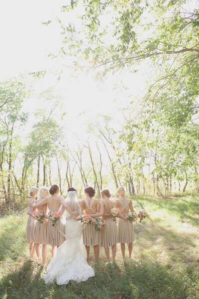 Bride and six bridesmaids outdoors wearing beige dresses with back detailing