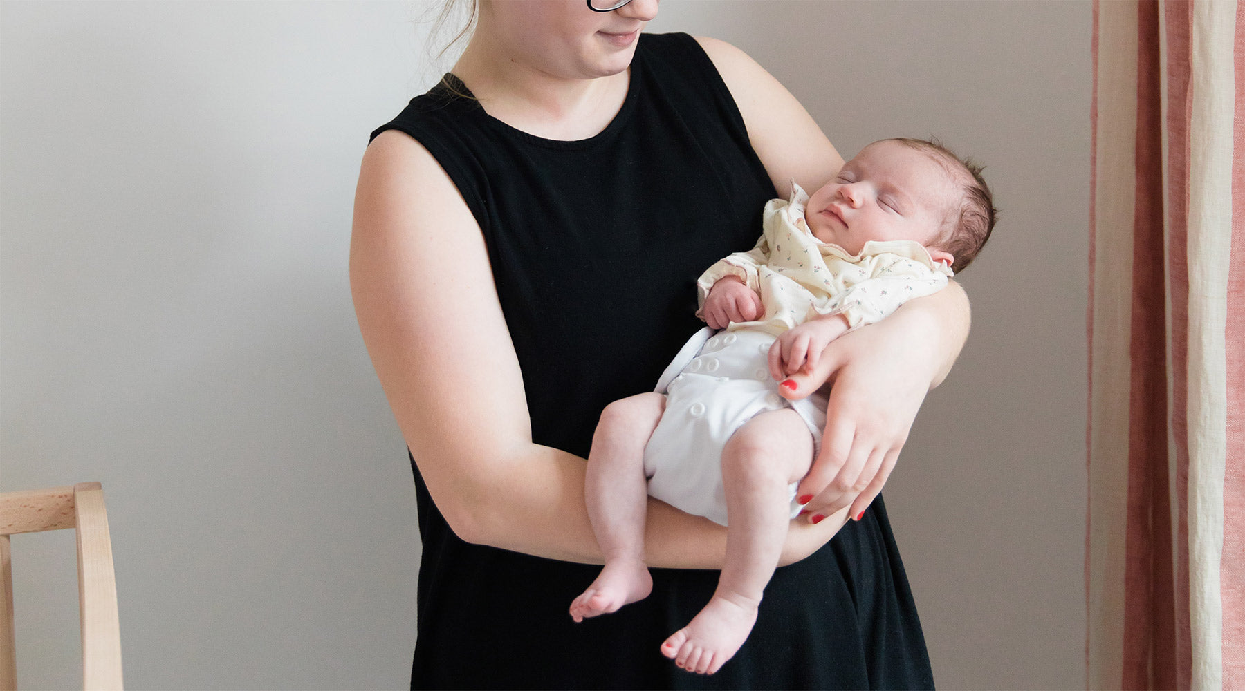 mom in black dress holding newborn baby in white cloth diaper cover