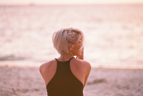 A girl with blonde hair sitting on the beach by the ocean.