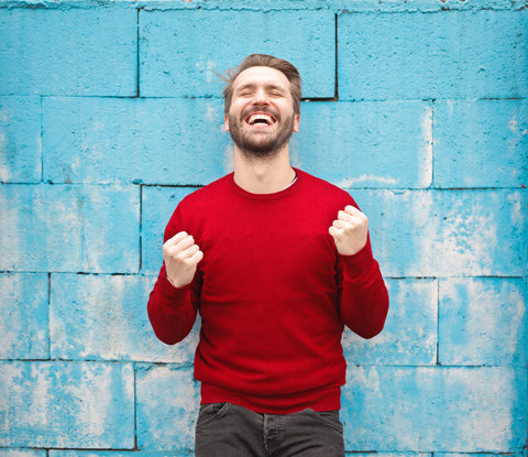 A happy man in a red shirt with a blue wall.