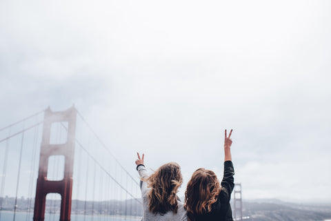 Two girls with their hands in the air by the Golden Gate Bridge.