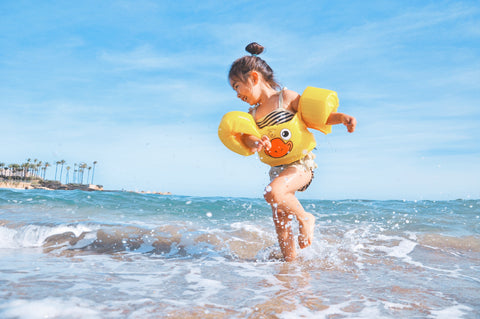 A girl with floaties playing in the ocean.