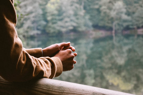 A man with his hands clasped by a lake.