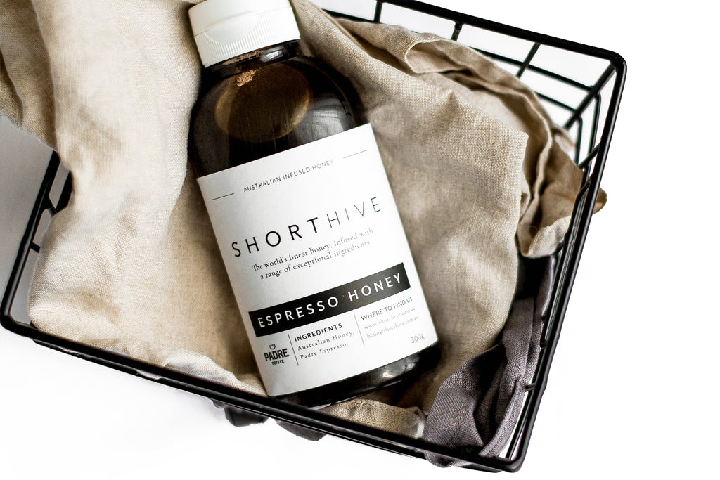 ShortHive espresso (coffee) honey bottle sitting in black wire basket on a grey tea towel