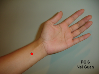 arm with hand open palm with red dot on the wrist representing acupressure point