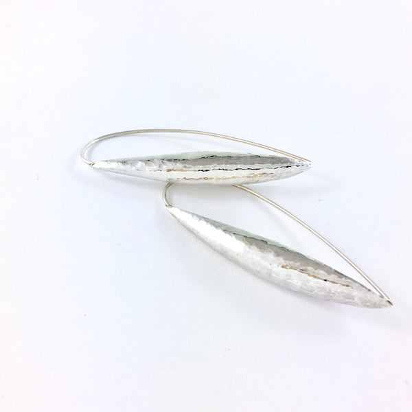 The Pod Earrings, organic in shape and texture, dramatic in appearance. Elongated thread hoop earrings with a tapered hand forged pod front. Hammered and polished. Made in solid Sterling Silver.
