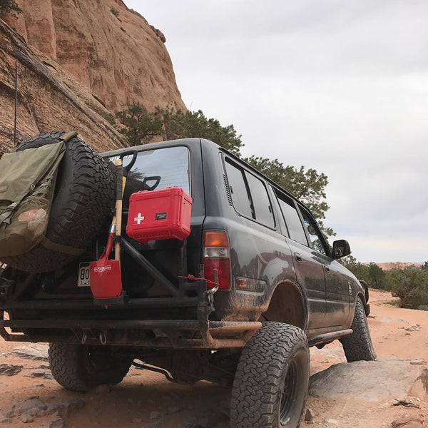 Off road first aid kit from outerlimit supply shown mounted next to spare tire and recovery shovel on 4x4 vehicle