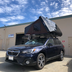 black Subaru Outback with black hardshell ikamper roof top tent installed in San Francisco Overland Outfitter Showroom