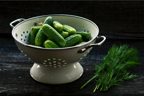 wet green small cucumbers in a strainer sitting on a counter