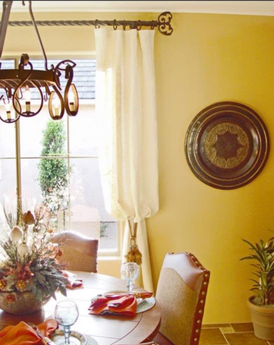 bright yellow walls in a country style dining room with intricate curtain rod and finial detail