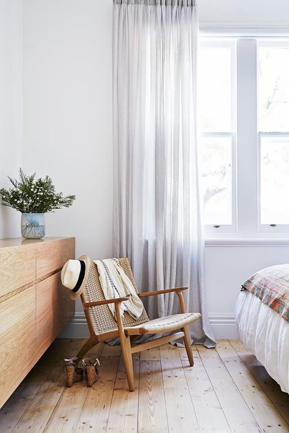 summery bedroom with woven chair wooden floors and grey curtains