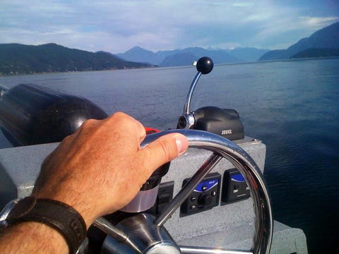 Image of a man's hand on the steering wheel of  boat with ocean and mountains ahead