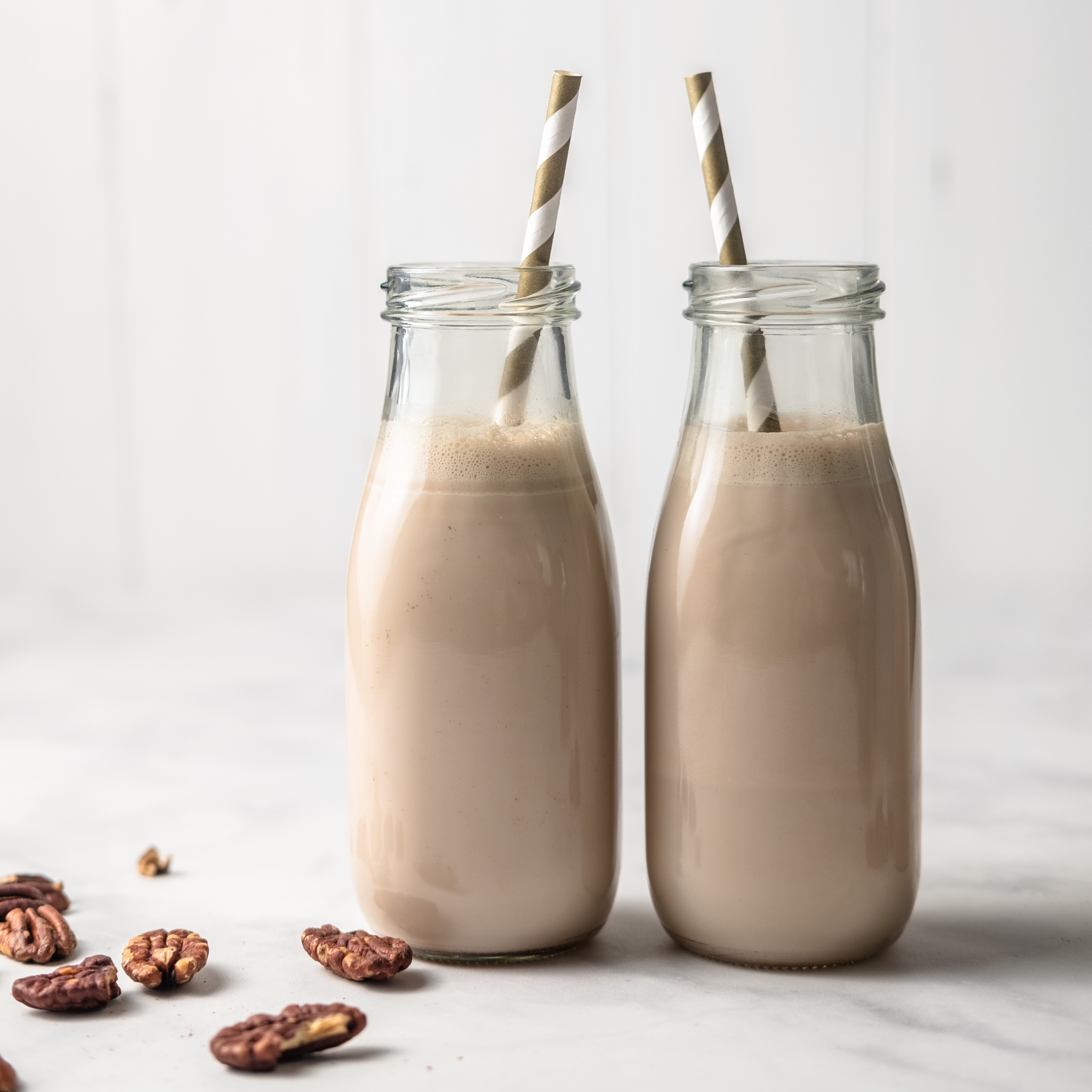 homemade pecan milk in two glasses with straws, next to pecans