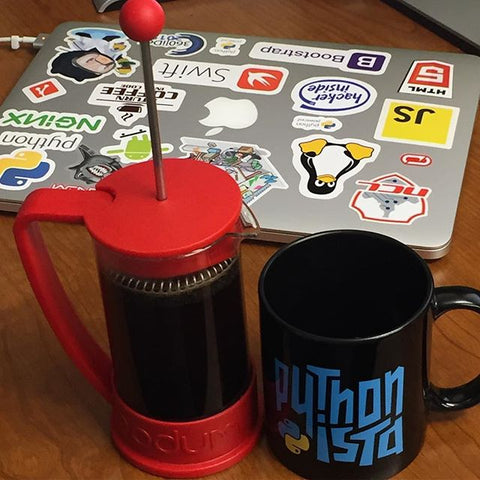 Pythonista Mug and a coffee maker in front of a laptop with stickers