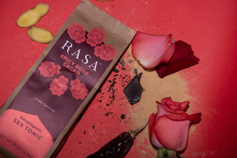 Spicy Rose Aphrodisiac Rasa with Maca powder, rose petals, chocolate, chiles, and ginger slices on red background