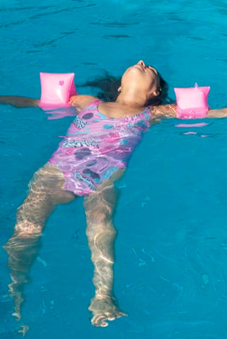 Woman wearing B Fresh All That Racket swimsuit floating in pool.