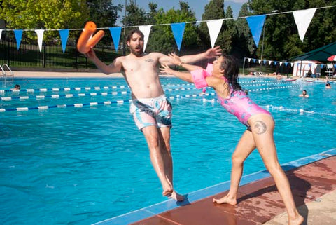 Woman wearing B Fresh All That Racket swimsuit pushing a man wearing B Fresh Cordial swimsuit into pool.