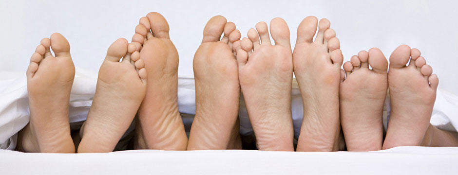 Bottom of bare feet in a row, out from under a sheet
