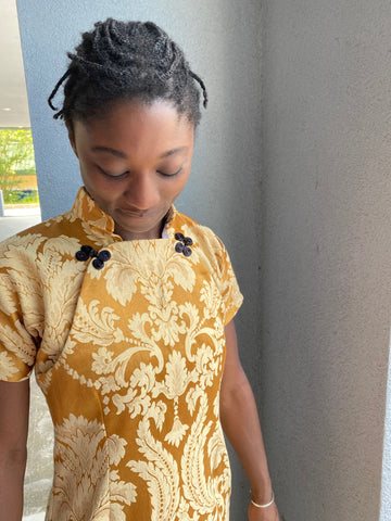 woman standing outside wearing a gold brocade Cheognsam