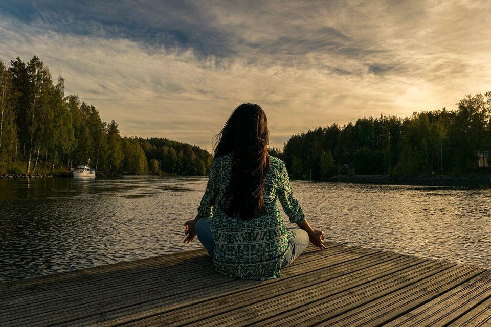  A woman sitting down meditating near a lake at twilight.