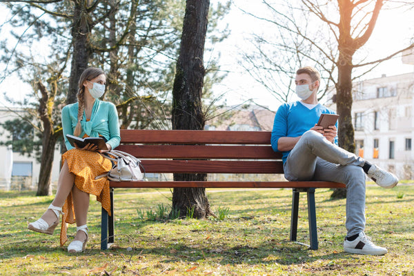 Homme et femme assis sur un banc avec distance de sécurité et masque facial