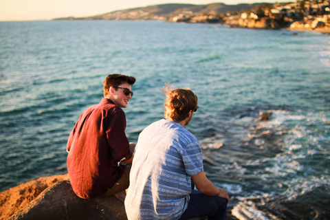 Two male friends chatting on a rock near the ocean