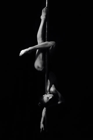Black and white photo of woman hanging upside down on a poll