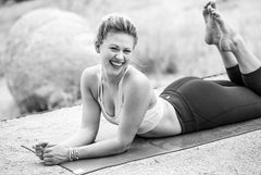 Young woman smiles while laying on her belly with her feet kicked up on a yoga mat image in black and white