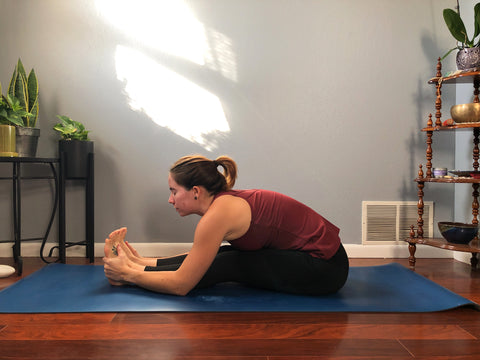 girl on yoga mat does a seated forward fold