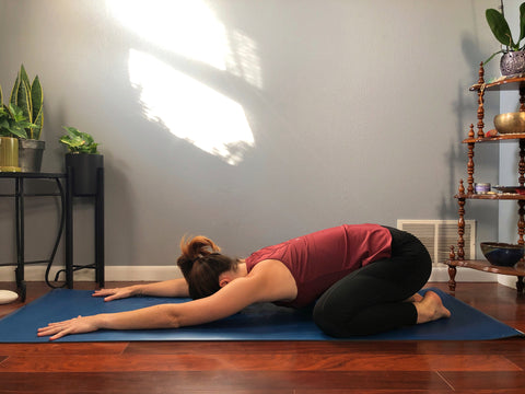 girl does childs pose on yoga mat