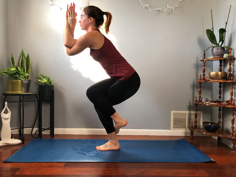 girl does eagle pose standing on a yoga mat