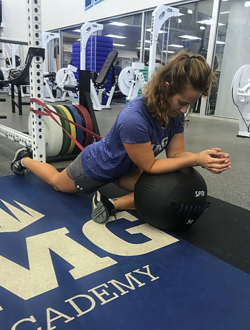 Woman  does pigeon pose at the gym using a SPRI Superband and Soft Shell Med Ball