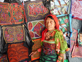 a kuna female artisan standing in front of the mola bags