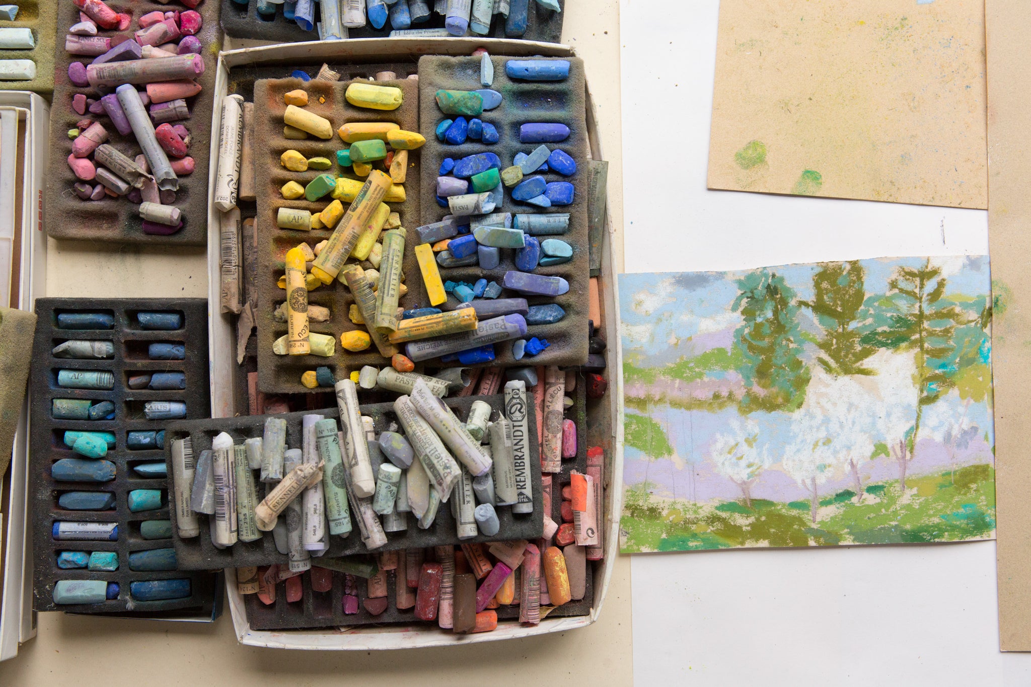 box of pastels next to pastel artwork on table